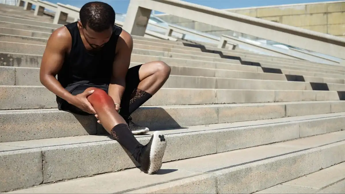 Can Shoes Cause Knee Pain. A runner sitting on stairs holding his knee due to knee pain