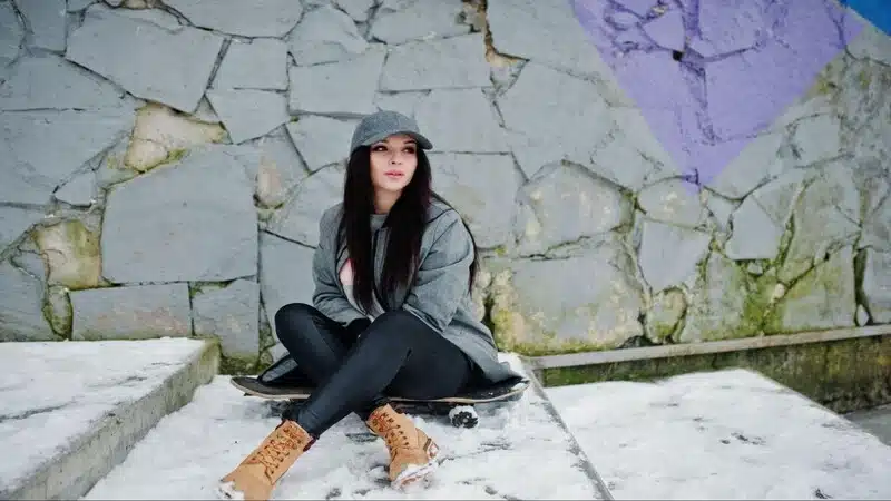 The picture show snow season and a girl setting on stairs wearing brown shoes and gray jacket